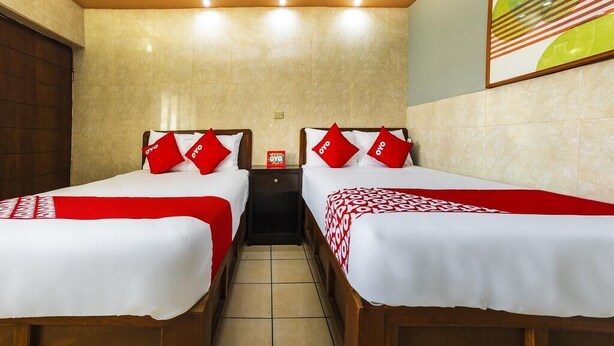 Quarto de hotel com duas camas, cada uma com colcha vermelha e branca e almofadas a combinar.
