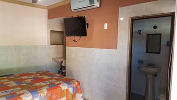 A hotel room with a bed, a television mounted on the wall, an air conditioning unit, a sink, and a mirror in the bathroom.