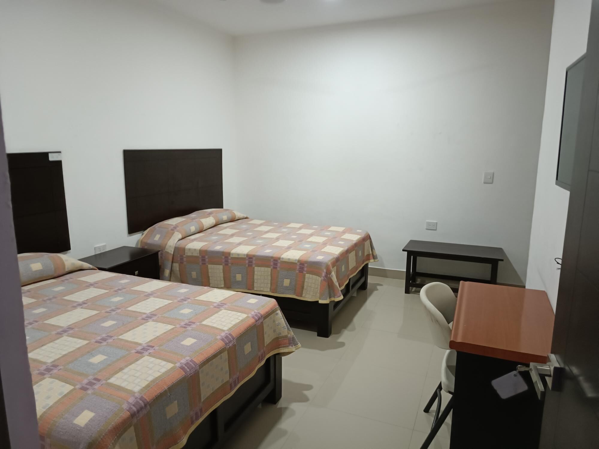 A hotel room with two beds, a desk, a chair, and a TV.