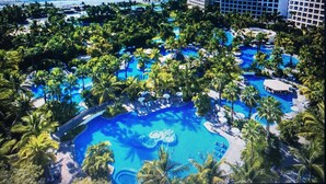 Un resort con una grande piscina circondata da palme e vista sull'oceano.