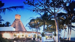 Un resort con un edificio principale con tetto di paglia, palme e un prato curato.