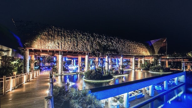 Un resort con una grande piscina, una struttura con tetto di paglia e sentieri ben illuminati.