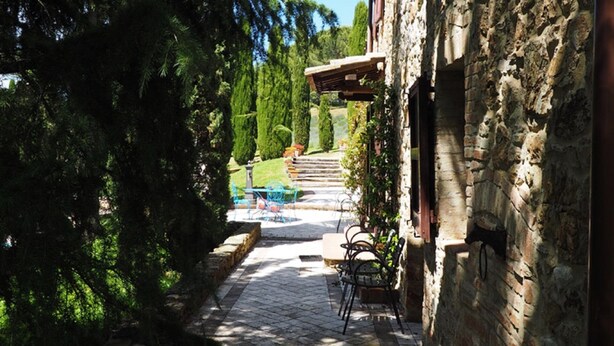 A stone building with a paved pathway leading to a seating area with chairs and a table. - Ginestra, house with outdoor patio and overlooking the common swimming pool (San Gimignano)