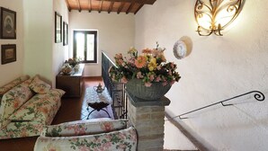 A cozy living room with floral-patterned sofas, a large vase of flowers on a staircase, and a wall-mounted light fixture. - Ginestra, house with outdoor patio and overlooking the common swimming pool (San Gimignano)