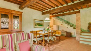 A dining area with a wooden table, chairs, and a striped sofa. There is a staircase with a green railing and a brick wall. - L'Aia, two bedrooms apartment in the Chianti area with A/C and swimming pool (Tavarnelle Val di Pesa)
