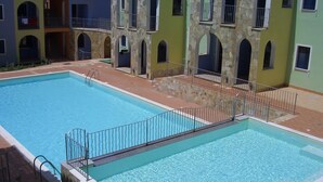 Una piscina con valla metálica de seguridad, rodeada de edificios de varios pisos con balcones y ventanas de arco.