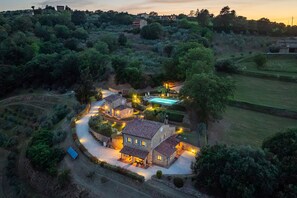 A stone villa with a swimming pool, surrounded by lush greenery and a winding path.