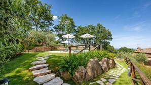 Ein Garten mit einem Kiesweg, Sitzgelegenheiten im Freien und Sonnenschirmen.
