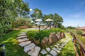 A garden with a stone pathway, outdoor seating, and umbrellas.