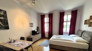 Un dormitorio con cama, un escritorio con computadora, una silla y una ventana con cortinas.