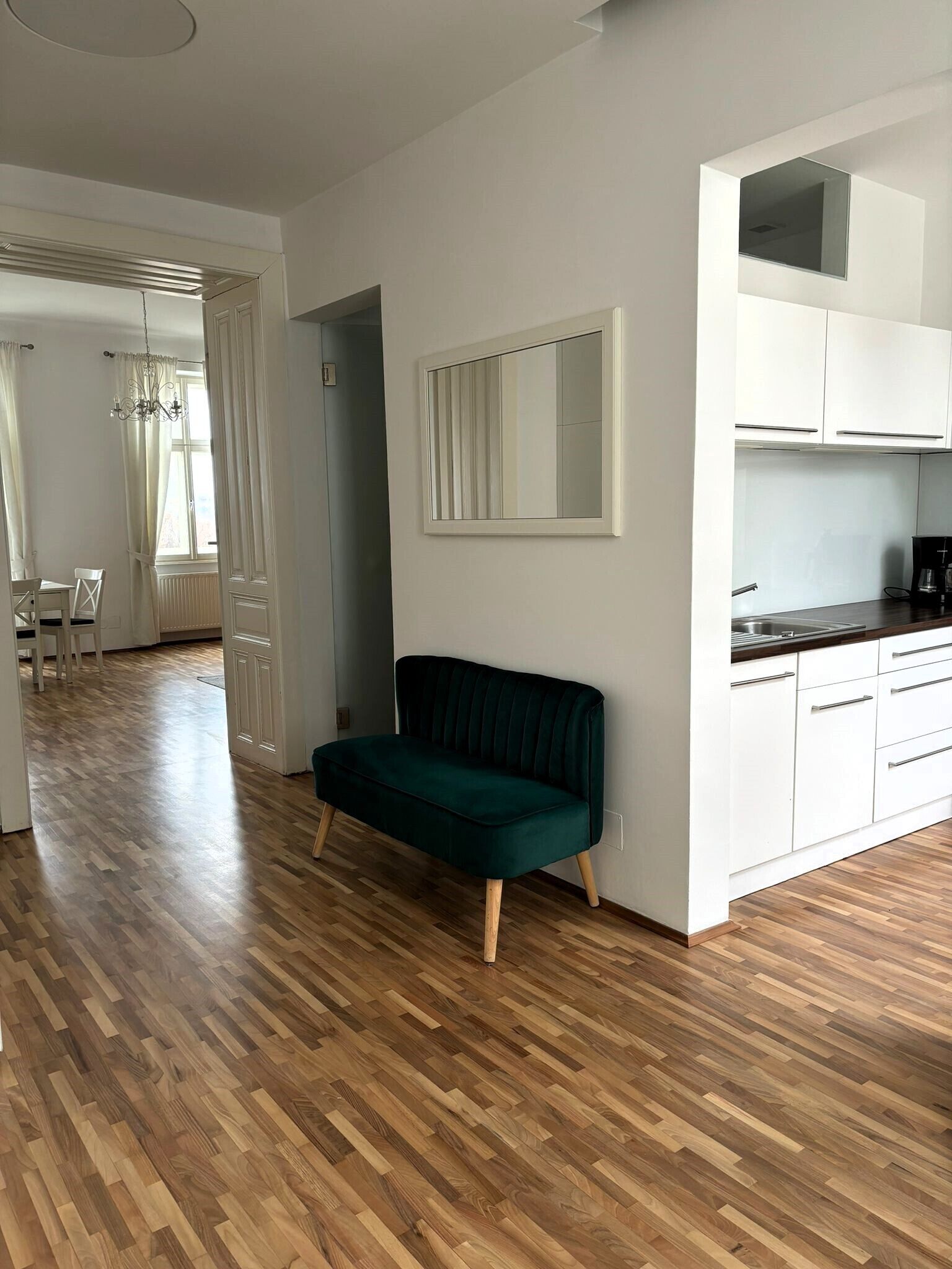 Eine moderne Wohnung mit Holzboden, einem grünen Sofa, weißen Schränken und einem Essbereich mit Tisch und Stühlen.
