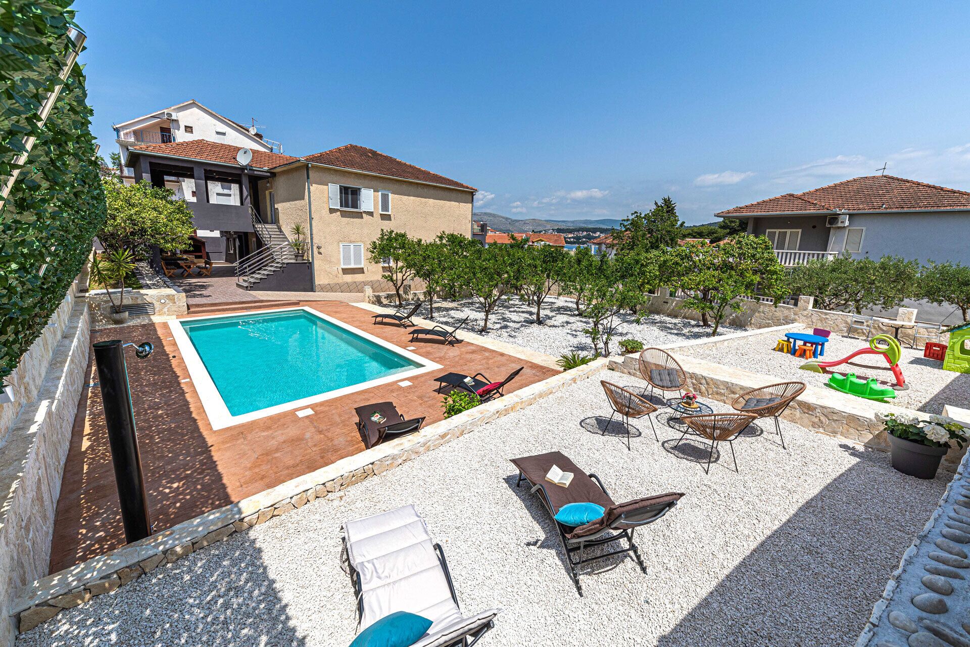Area piscina con lettini e un tavolo, circondata da un patio in ghiaia e vista sul mare.