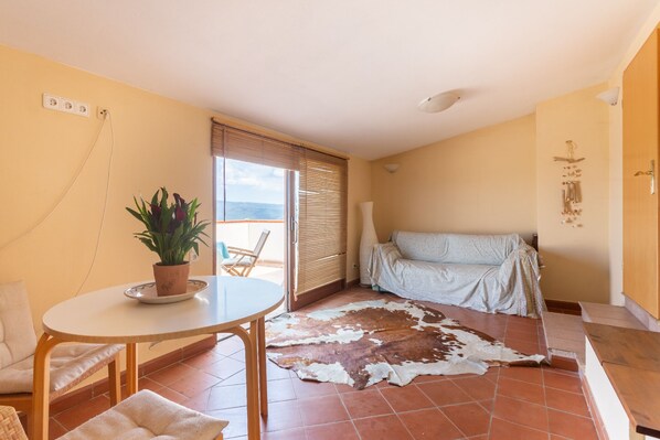 A room with a round table, a sofa, a potted plant, and a large cowhide rug.