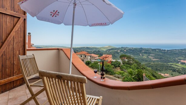 A balcony with a white umbrella, two wooden chairs, and a bottle of wine. - Our sea view house offers space on 400 square meters for 2-10 people (Magomadas (OR))