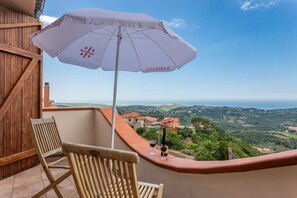 A balcony with a white umbrella, two wooden chairs, and a bottle of wine.