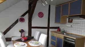 Un comedor con una mesa de madera, sillas blancas y una cocina con armarios azules y una estufa.