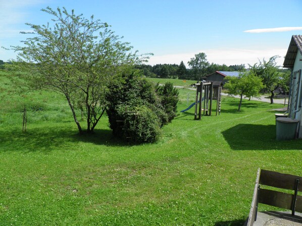 Un espacio al aire libre con césped, una estructura de juegos, un banco y un edificio al fondo.