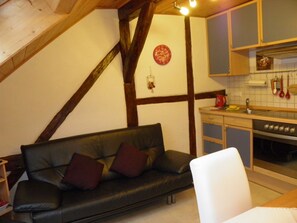 Un espacio de sala acogedor con un sofá de cuero negro, techo de madera y cocina con estufa y utensilios colgantes.