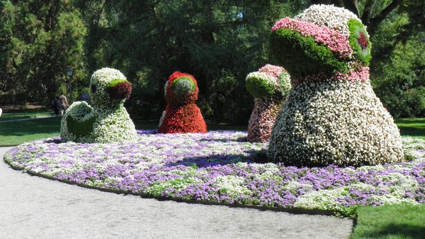 Un jardín con esculturas de animales hechas con setos topiarios, rodeado de macizos de flores.