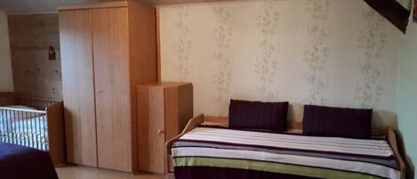 A bedroom with a bed, a wooden wardrobe, and a crib.
