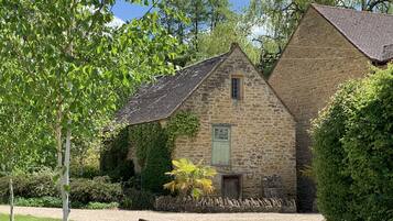 A stone building with a sloped roof, surrounded by greenery and a gravel path.