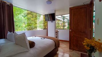 A hotel room with a bed, a TV mounted on the wall, a window with a view of greenery, and a door.