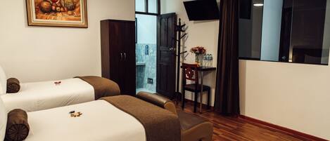 A hotel room with two beds, a desk with a chair, a TV, and a painting on the wall.