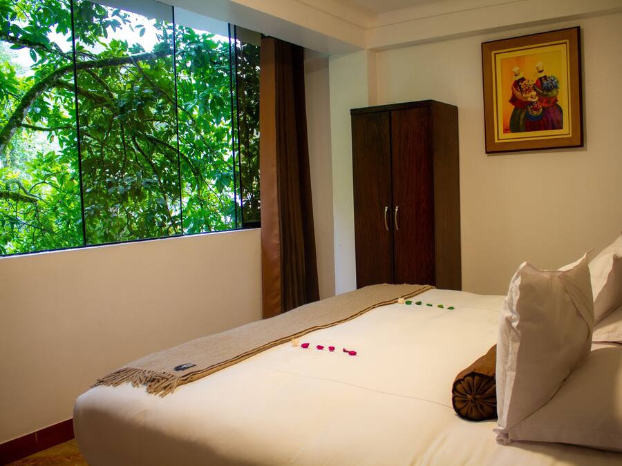 A bedroom with a large window, a bed with white linens, a wooden wardrobe, and a framed picture on the wall.