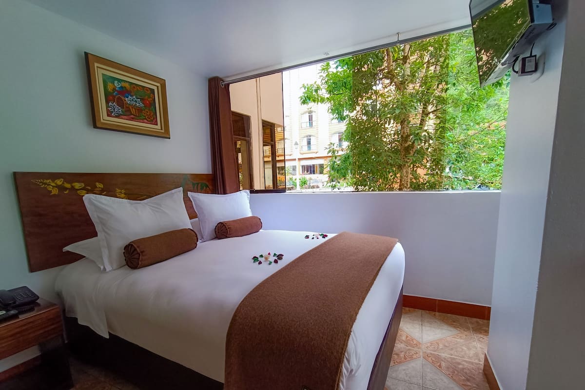 A hotel room with a bed, a nightstand, a painting, and a view of the outside.