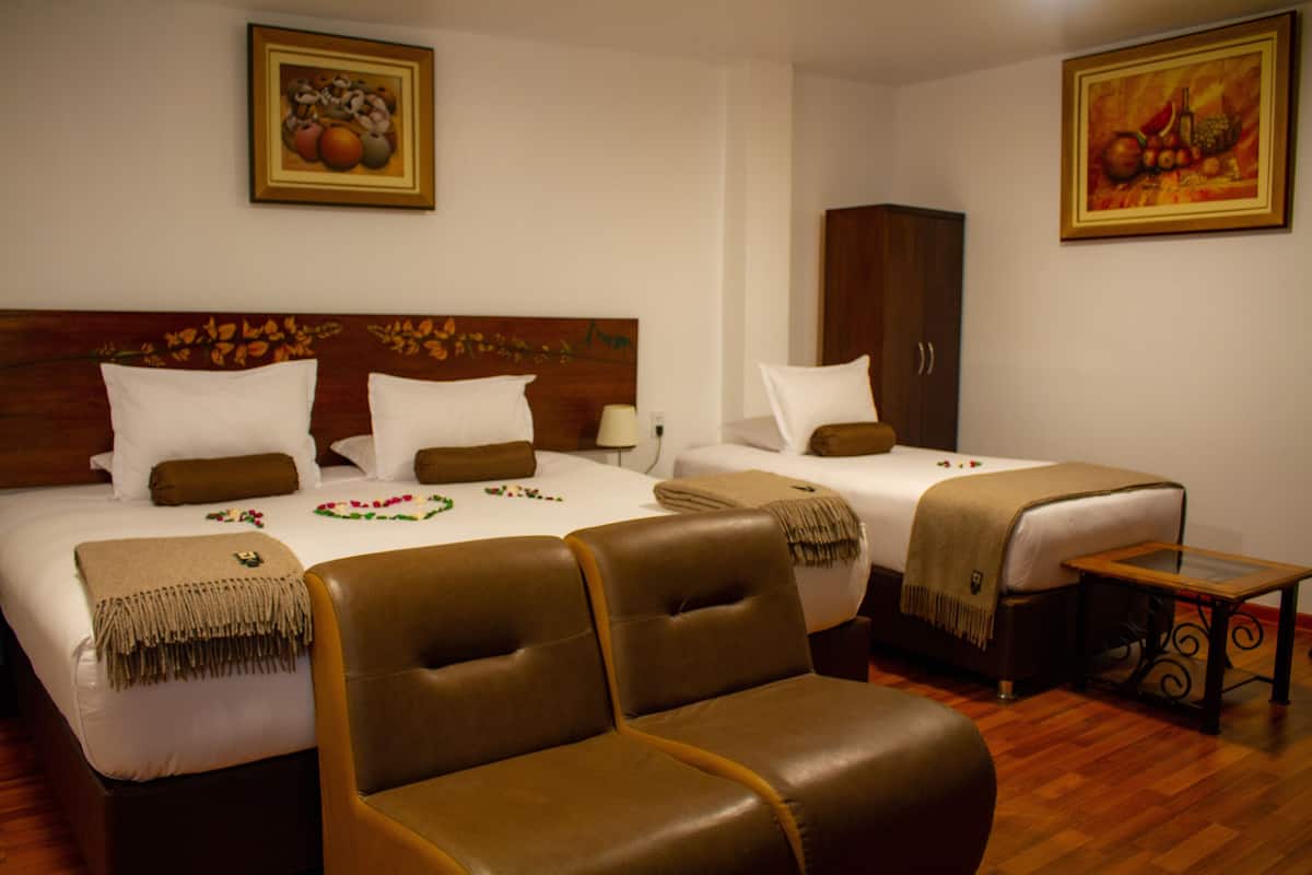 A hotel room with two beds, a wooden headboard, a brown leather chair, a small wooden table, and two paintings on the walls.