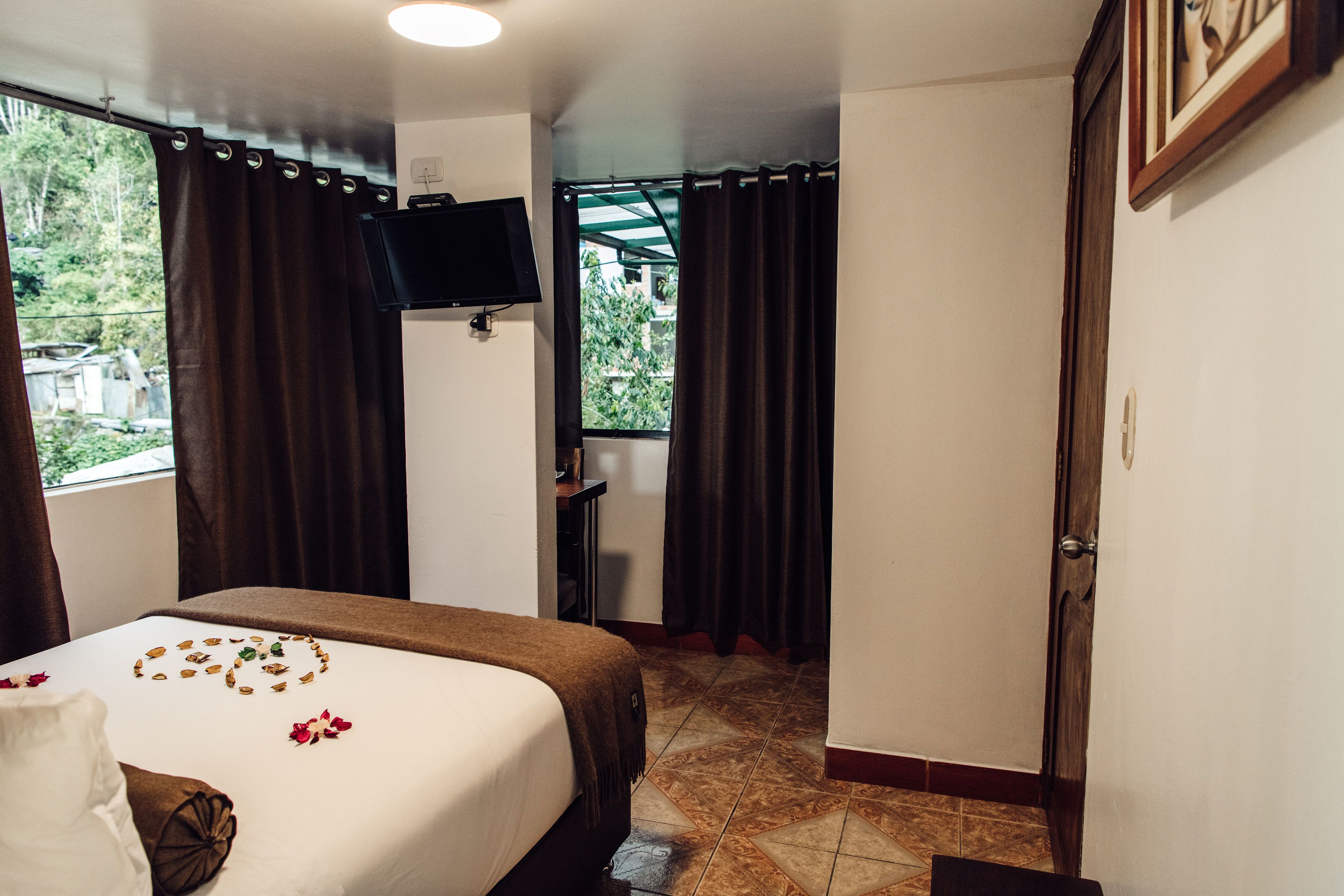 Habitación de hotel con cama, televisor, escritorio y ventana con cortinas.
