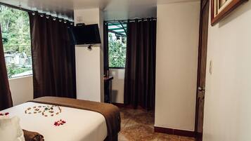 Habitación de hotel con cama, televisor, escritorio y ventana con cortinas.