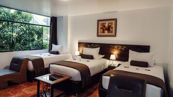 Habitación de hotel con dos camas, un espacio de descanso y vistas a la vegetación a través de amplios ventanales.