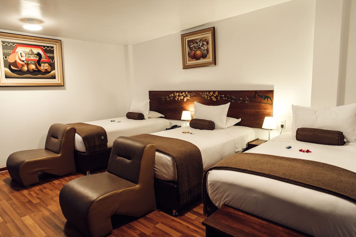 A hotel room with two beds, a sofa, and a wooden floor.