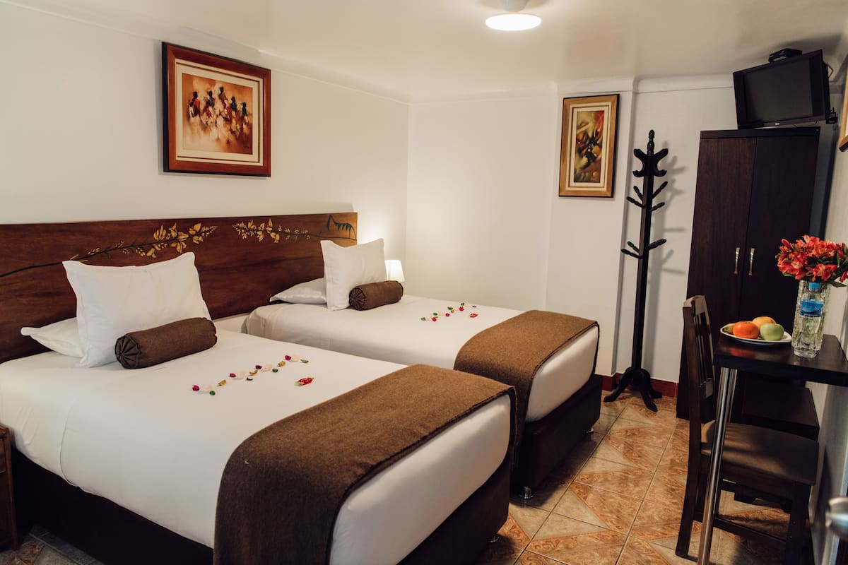 A hotel room with two beds, a wooden headboard, a television on a cabinet, and a table with a water bottle and fruit.