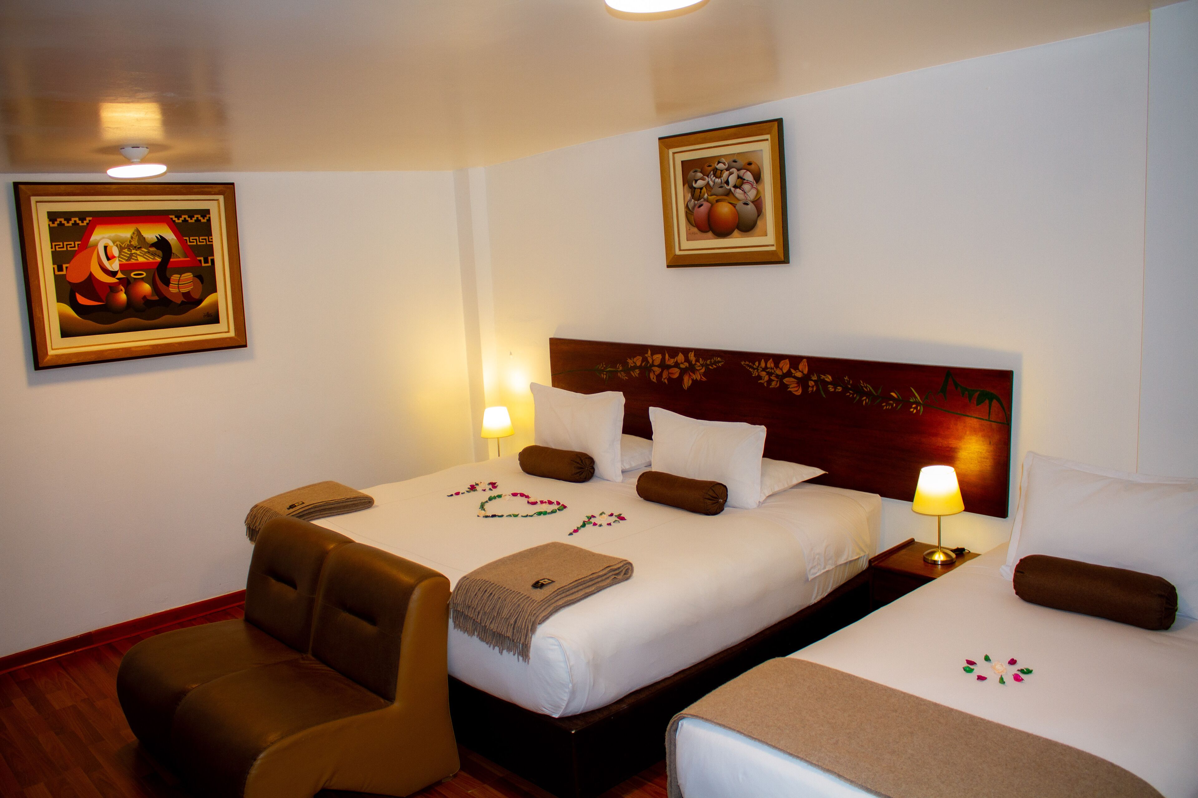 A hotel room with a large bed, two bedside tables, a chair, and two paintings on the walls.