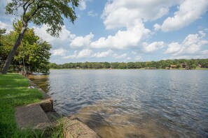 Un lac paisible, bordé d’une rive herbeuse, avec une falaise rocheuse et un arbre.