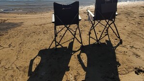 Zwei Strandstühle mit Blick auf einen See unter blauem Himmel.