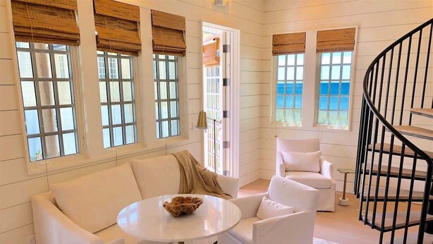 A modern interior with a white sofa set, a round table, and a spiral staircase.