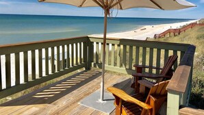 A wooden deck with a white umbrella, wooden chairs, and a view of the beach.