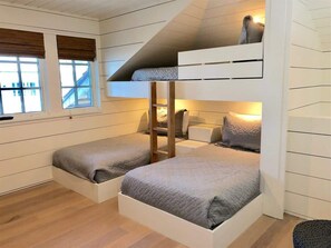 Ein Mehrbettzimmer mit einer Klappleiter, zwei Betten, einem Fenster mit Jalousien und Holzboden.