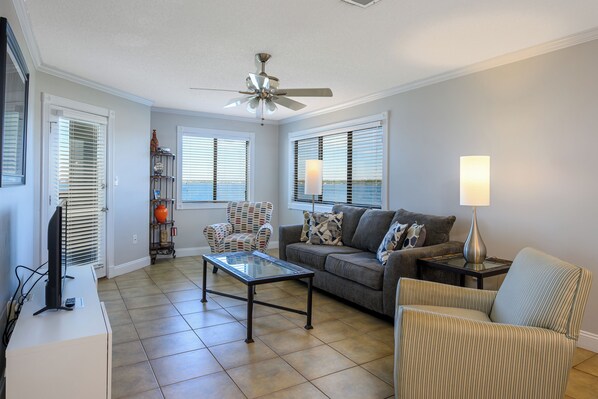 A living room with a ceiling fan, a sofa, a coffee table, and a TV. - Your Sound Side Sanctuary Awaits in Palms 1-206 (Gulf Breeze)