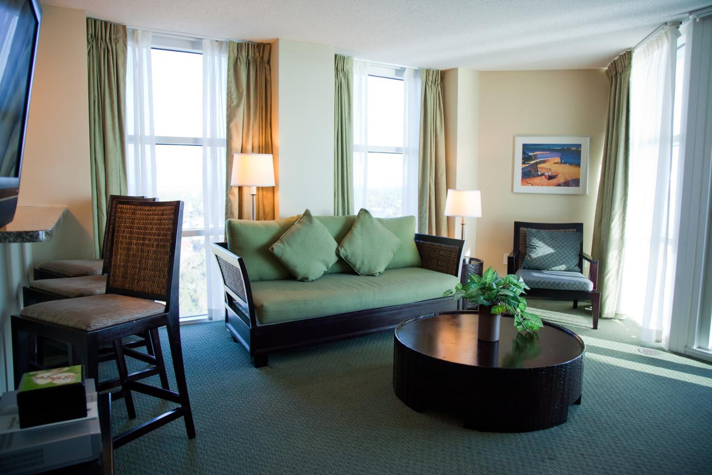 A hotel room with a green sofa, two chairs, a round coffee table, and a painting on the wall.