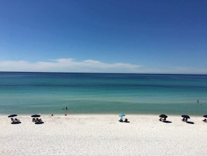A beach with white sand and clear blue water. There are umbrellas and lounge chairs along the shore.