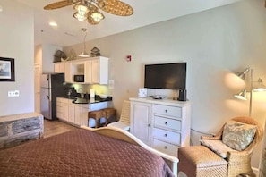 A compact room with a bed, kitchenette, TV, and a chair.