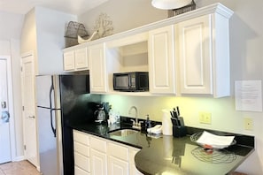 A kitchen with white cabinets, a black countertop, a microwave, a refrigerator, and a sink.
