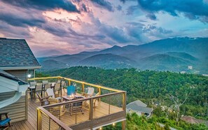 Una terraza de madera con mobiliario exterior y una chimenea, con vistas a un paisaje montañoso.