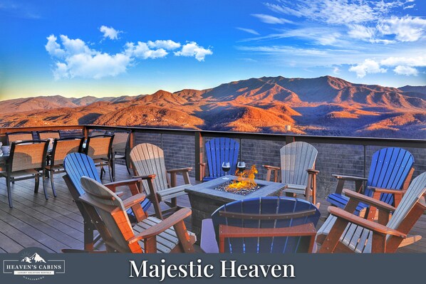 Una terraza con sillas Adirondack y un brasero, con vistas a un paisaje montañoso.