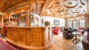 Een houten barruimte met flessen en glazen op planken, een zithoek met banken en tafels, en een groot raam met uitzicht.