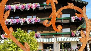 Een rustiek hotel met een houten gevel, bloembakken op de balkons en een decoratieve metalen hartvormige constructie op de voorgrond.
